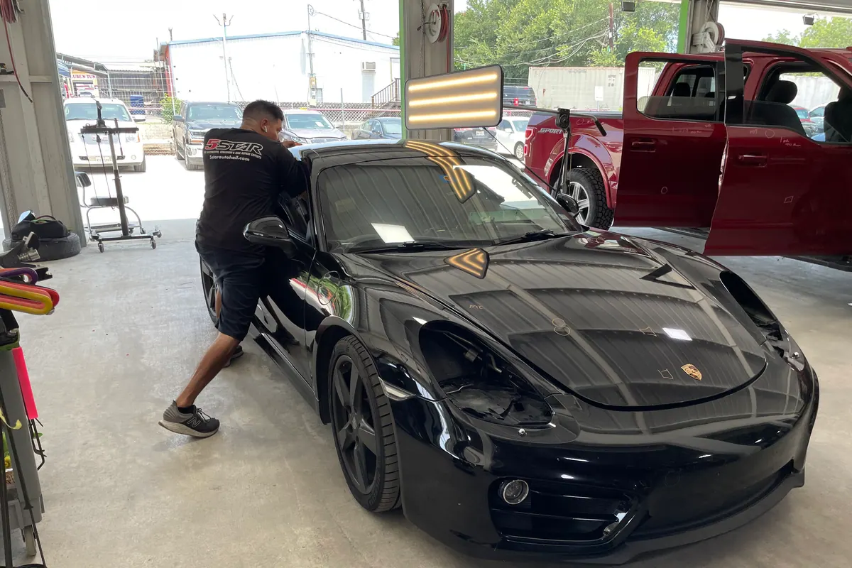 Technician completing paintless dent repair on a black Porsche