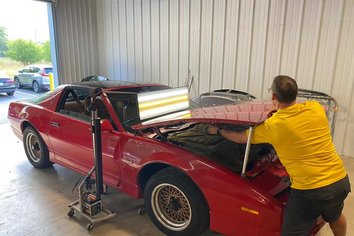 Technician using a reflection light on a red classic car