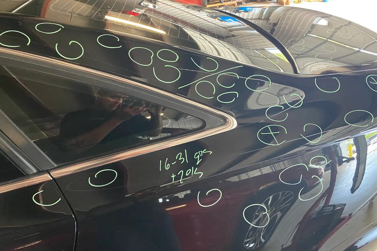 Hail dents individually marked across a vehicle roof and pillar