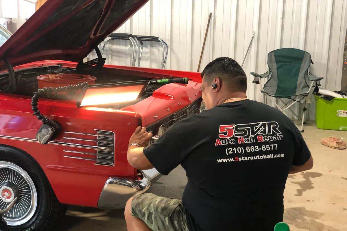 Technician repairing the front fender of a red classic car